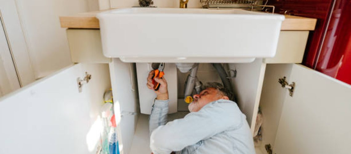 Mature man solving plumbing problems in a kitchen